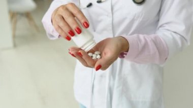 Beyaz önlüklü kıdemli bayan doktor kavanozdan hap alıyor. Ellerin görüntüsünü kapat