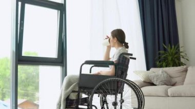 Tekerlekli sandalyede oturan kadın evde kitap okuyor.
