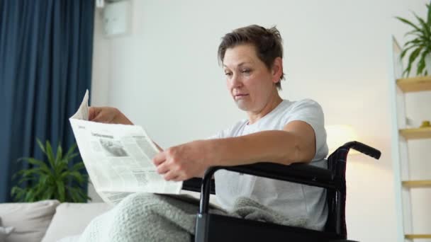 老年妇女坐在轮椅上 在家里看报纸 — 图库视频影像