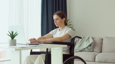 Motivasyonlu serbest yazar evde tekerlekli sandalyede oturup dizüstü bilgisayarla yazı yazıyor. Uzak çalışma konsepti