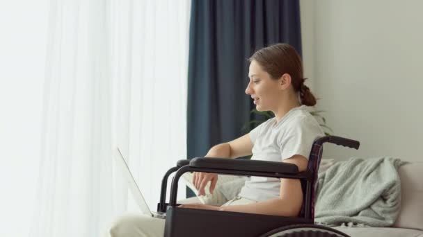 モチベーションの高いフリーランスは 自宅の車椅子に座ってノートパソコンを入力して作業しています 遠くの仕事の概念 — ストック動画