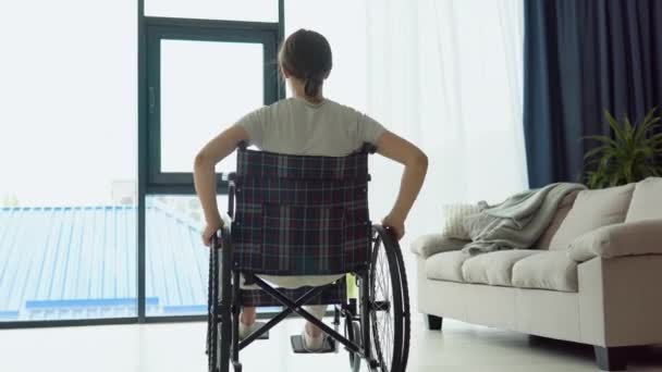 Uma Jovem Mulher Uma Cadeira Rodas Dirige Até Janela Olha — Vídeo de Stock