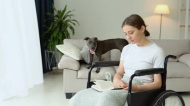 Tekerlekli sandalyede oturan kadın evde kitap okuyor.