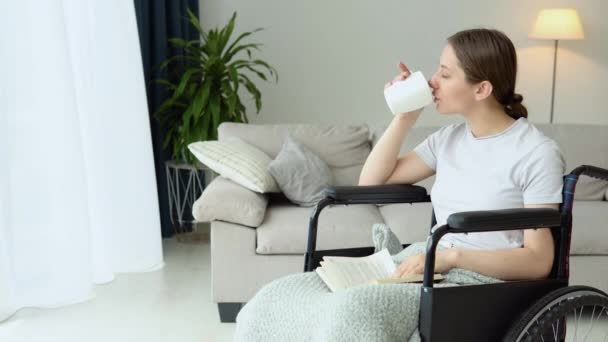 車椅子に座って本を読んで家でコーヒーを飲む若い女性 — ストック動画
