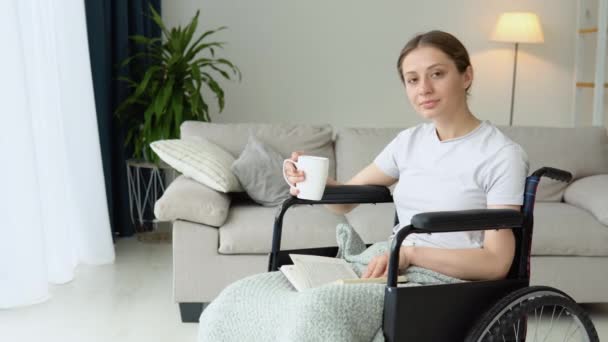 年轻女子坐在轮椅上看书 在家里喝咖啡 — 图库视频影像