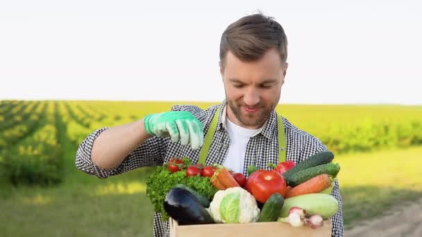 新鮮な収穫野菜と幸せな農家のバスケットを保持し 田舎のフィールドにカメラで笑顔 コンセプト 生物学 バイオ製品 生物生態学 菜食主義者やビーガン — ストック動画