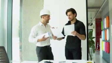 Two businessman engineers working in bright clean office. Discussing the construction project, plan, drawing, scheme