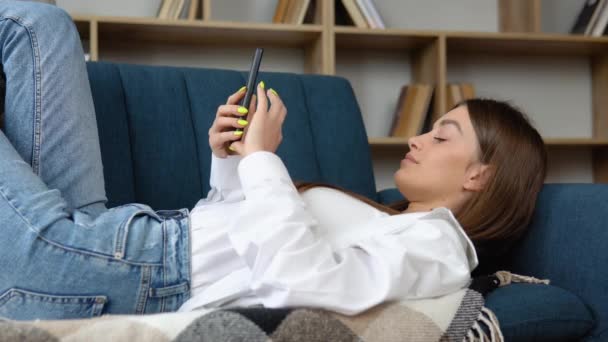 Улыбающаяся Красивая Девушка Отдыхает Дома Диване Используя Мобильный Телефон — стоковое видео