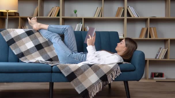 Mooie Glimlachende Vrouw Die Een Boek Leest Bank Woonkamer Ligt — Stockvideo