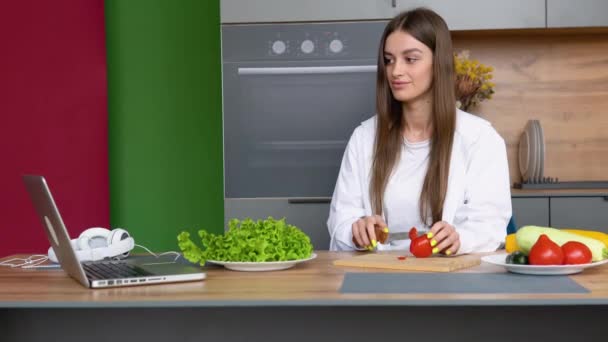 キッチンテーブルのキッチンノートパソコンや料理の女の子でラップトップでレシピを探して料理を楽しんで幸せな美しい若い女性 フードブロガーコンセプト — ストック動画