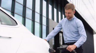 Sakallı adam elektrik tedarikçisini elektrikli arabaya bağlıyor. Ekolojik modern elektrikli araçların işlem şarjı. Ulaşım için alternatif enerji.