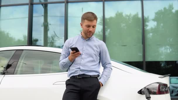 Mężczyzna Trzymający Smartfona Pobliżu Ładowania Samochodu Elektrycznego Samochód — Wideo stockowe
