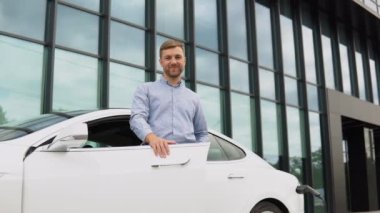 Man charging electric car near the business centre.