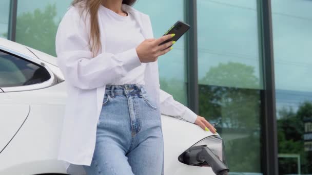 Korzystanie Smartfona Podczas Oczekiwania Kobieta Stacji Ładowania Samochodów Elektrycznych Ciągu — Wideo stockowe
