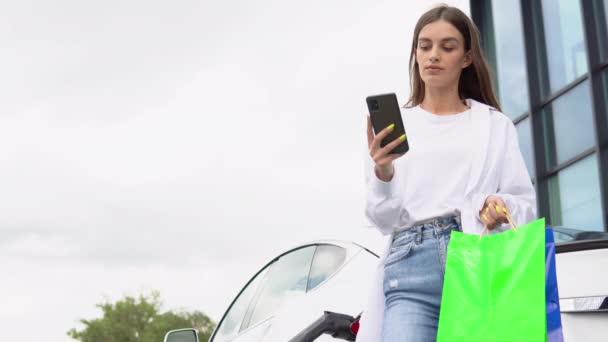Young Girl Buying Products Shopping Bag Standing Charging Electric Car — Vídeos de Stock
