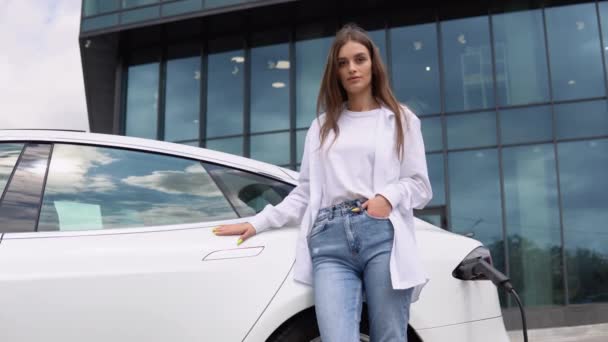 Lachende Jonge Blanke Meisje Pluggen Elektriciteitskabel Elektrische Auto Voor Het — Stockvideo