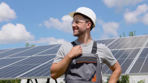 太阳能电池农场行业自信工程师的肖像 员工对太阳能电池面板的安装有信心 站在太阳能电池板附近的戴防护头盔的男工的近照 — 图库视频影像