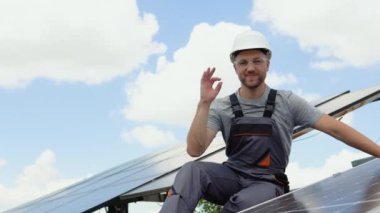 Male engineer in protective helmet installing solar photovoltaic panel system using screwdriver. Electrician mounting blue solar module on roof of modern house. Alternative energy ecological concept