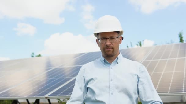 太阳能电池农场行业自信工程师的肖像 员工对太阳能电池面板的安装有信心 站在太阳能电池板附近的戴防护头盔的男工的近照 — 图库视频影像