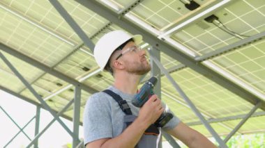 Male engineer in protective helmet installing solar photovoltaic panel system using screwdriver. Alternative energy ecological concept