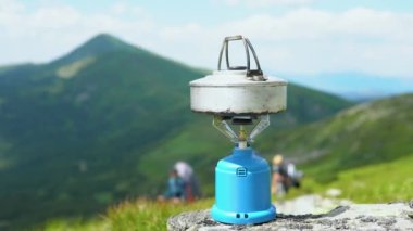 Camping kettle is on portable camping gas stove, water is heated, camping. At top of the hill against the background of the mountain close-up. Making tea or coffee.