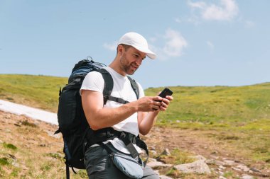 A bearded traveler with a backpack on the top of a mountain. A tourist with a backpack stands against the background of a mountain