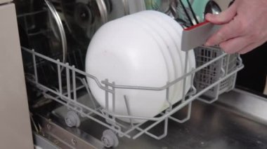 Young man loading dirty dishes into a dishwasher machine. A man uses modern appliance to keep the home clean. Close-up, top view.