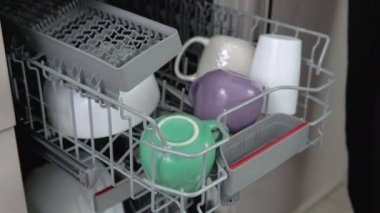 Young man loading dirty dishes into a dishwasher machine. A man uses modern appliance to keep the home clean. Close-up, top view.