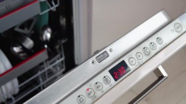 The girl chooses the dishwashing program on the dishwasher built into the kitchen and then closes the dishwasher cover