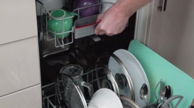 Young man loading dirty dishes into a dishwasher machine. A man uses modern appliance to keep the home clean. Close-up, top view.