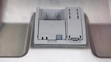 A womans hand puts a dishwasher pill in a close-up dishwasher in the kitchen