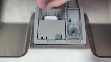 A mans hand puts a dishwasher pill in a close-up dishwasher in the kitchen.