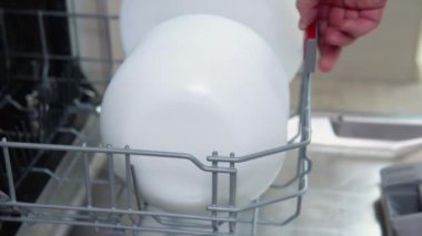 House chores concept. A man taking out clean plates from dishwasher machine. Male hands unloading dishwasher close up. Modern technologies for home.