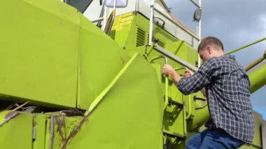 Driver go combine cabin at sunset. Professional agronomist working on harvesting autumn campaign. Unrecognized farmer operator getting into harvester inspecting machine. Agribusiness worker concept.