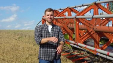 Farmer in wheat field holding digital tablet and showing thumb up. He is smiling. Combine harvester harvesting in background