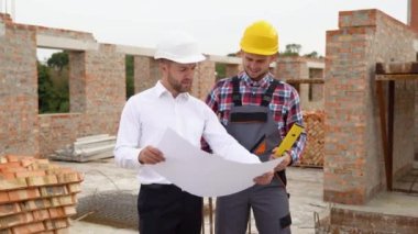 İki uzman ticari, endüstriyel inşaat alanını inceliyor. İnşaat mühendisiyle emlak projesi. Arka plandaki vinçte, gökdelen beton biçimlendirme çerçeveleri