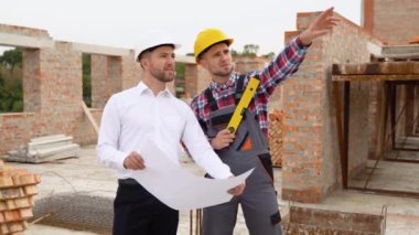 İki inşaat işçisi ev inşaatındaki mimari çizimlere bakıyor..