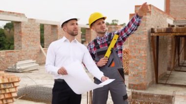 Two specialists inspect commercial, industrial building construction site. Real estate project with civil engineer.