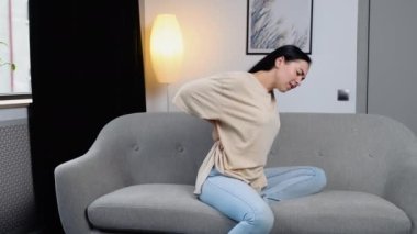 İnsanlar, sağlık ve sorun konsepti - mutsuz genç kadın sırt ağrısı çekiyor ya da evde dizginleniyor.