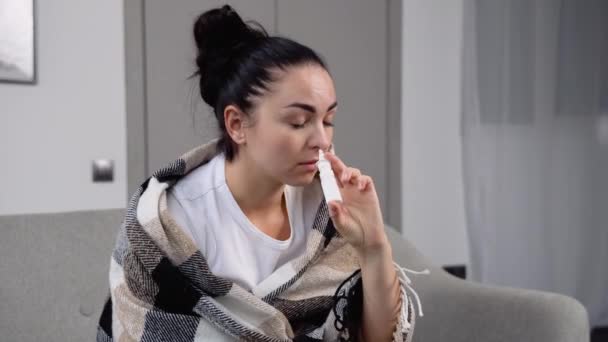 ソファに座っている間に毛布に包まれた若い女性は鼻スプレーをスプレーします — ストック動画