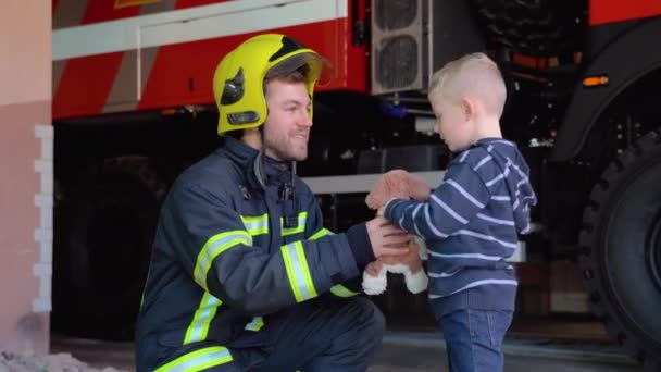 Mutiger Feuerwehrmann Uniform Und Kleiner Junge Mit Spielzeug Vor Dem — Stockvideo