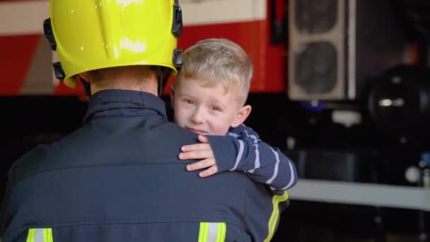 Храбрый Пожарный Форме Держит Маленького Спасенного Мальчика Стоящего Фоне Пожарной — стоковое видео