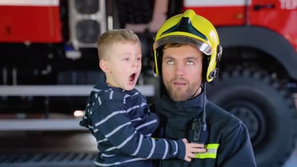 Rolig Brandman Uniform Håller Liten Rolig Pojke Mot Bakgrund Brandbil — Stockvideo