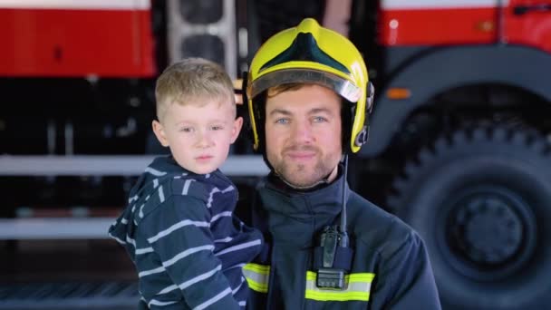 Odważny Strażak Mundurze Trzymający Małego Ocalałego Chłopca Tle Wozu Strażackiego — Wideo stockowe