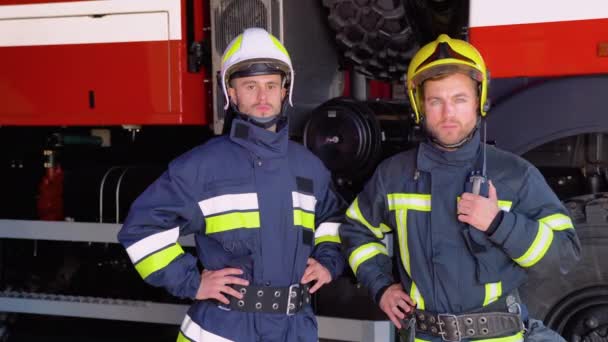 Два Пожарных Стоят Вместе Униформе Защитных Шлемах Пожарные Машины Заднем — стоковое видео