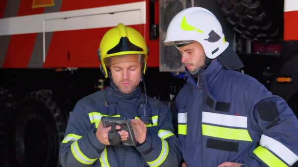 2人の消防士が消防車の外に立ってタブレットを手にし 消火のために何をすべきかを決める — ストック動画