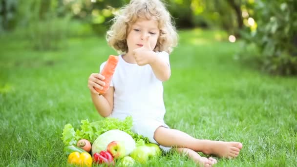 Счастливый ребенок ест овощи в весеннем парке. Концепция здорового питания — стоковое видео