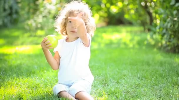 Happy child eating green apple in spring park. Healthy lifestyle concept — Stock Video