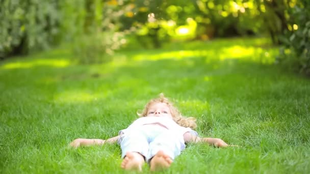 Happy child lying on green grass in spring park. Healthy lifestyle concept — Stock Video