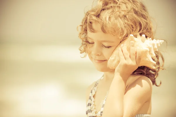 Gelukkig kind luisteren naar een zeeschelp op het strand — Stockfoto